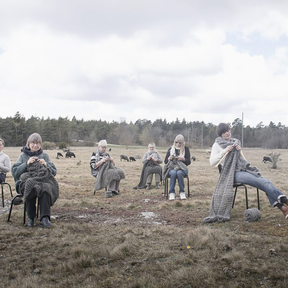 Handarbetare som sitter på stolar och stickar i fårhagen.